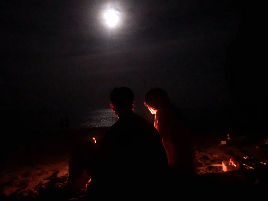 Camping by the fire with a bright moon over the ocean